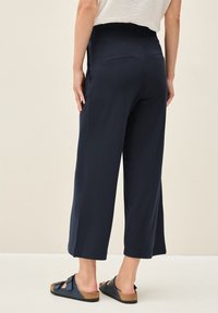 Navy wijde broek met een elastische tailleband en twee achterzakken, gecombineerd met zwarte sandalen. Soepele stof en een relaxte pasvorm.