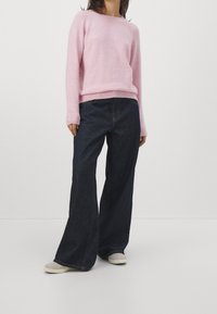 Ljusrosa stickad tröja med rundad halsringning och ribbade ärmslut, kombinerat med vida mörkjeans och beigea slip-on skor.