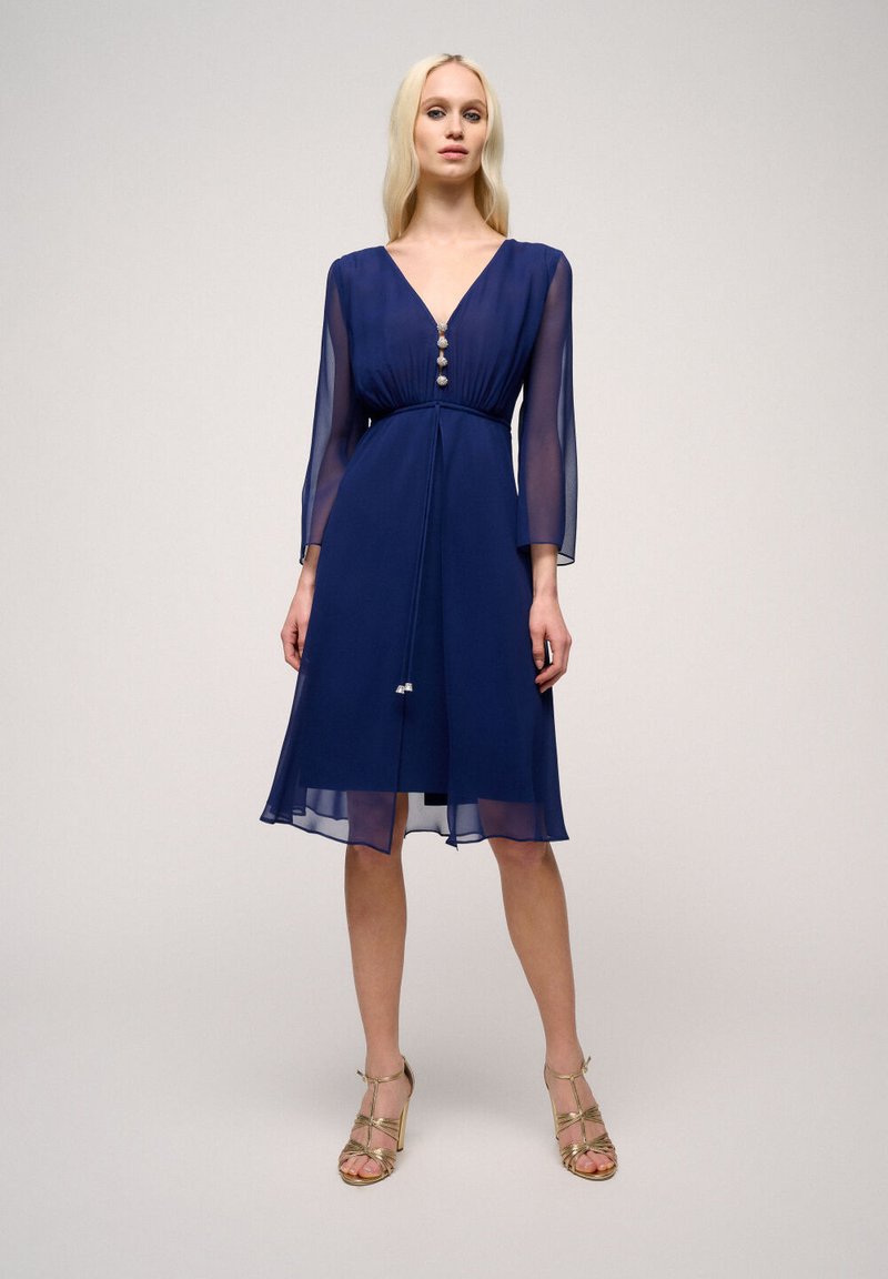 Navy blue chiffon dress with a v-neckline, three-quarter sleeves, button detailing, and a cinched waist, featuring a flowy hemline.