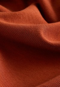 Strukturerat, stickat tyg i en varm, bränd orange färg. Har en lätt, mjuk känsla med synligt ribbat mönster och subtilt sken.