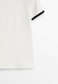 Chemise blanche à manches courtes avec bordure noire sur le poignet, présentée sur fond blanc.