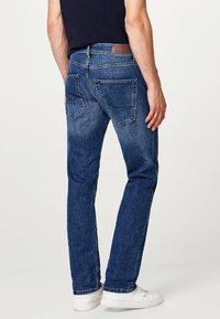 Mörkblå denimbyxor med rak bendesign, featuring två bakfickor och en läderlogotyp på midjan.