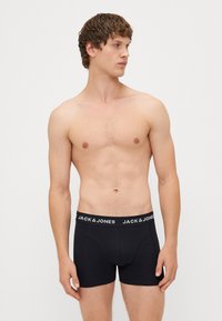Črne bokserice z logotipnim pasom, ki vsebuje "JACK & JONES" v beli barvi. Iz bombažnega materiala, prileganja, dolžina nad kolenom, gladka tekstura.