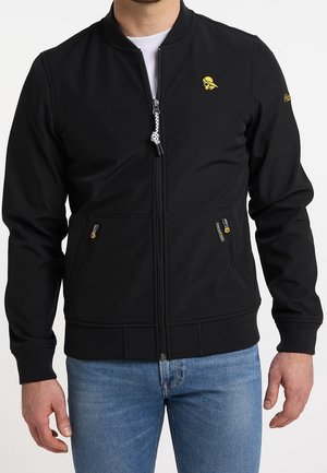 Mężczyzna w czarnej kurtce zapinanej na zamek z prążkowanymi mankietami i obszyciem na dole, z żółtym logo czaszki na piersi, kieszeniami z przodu na zamek, w parze z niebieskimi dżinsami.