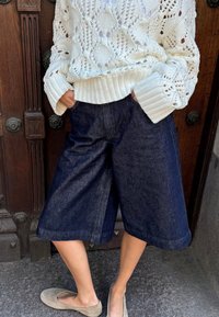 Tumed denim culotid, mis on paari pandud tekstuuriga valge kudumisega sviitriga, millel on laiad sääred ja kontrastsete soonikkoes varrukad.