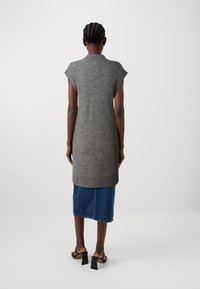 Túnica sin mangas gris de punto con cuello y dobladillo acanalados, combinada con una falda vaquera. Sandalias negras de tacón alto completan el conjunto.