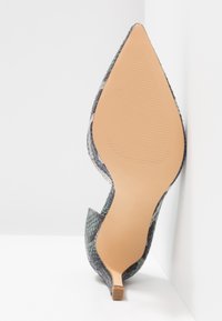 Chaussure à talon haut à bout pointu avec un motif peau de serpent gris et noir texturé, montrant une semelle beige lisse et une fine pointe de talon.