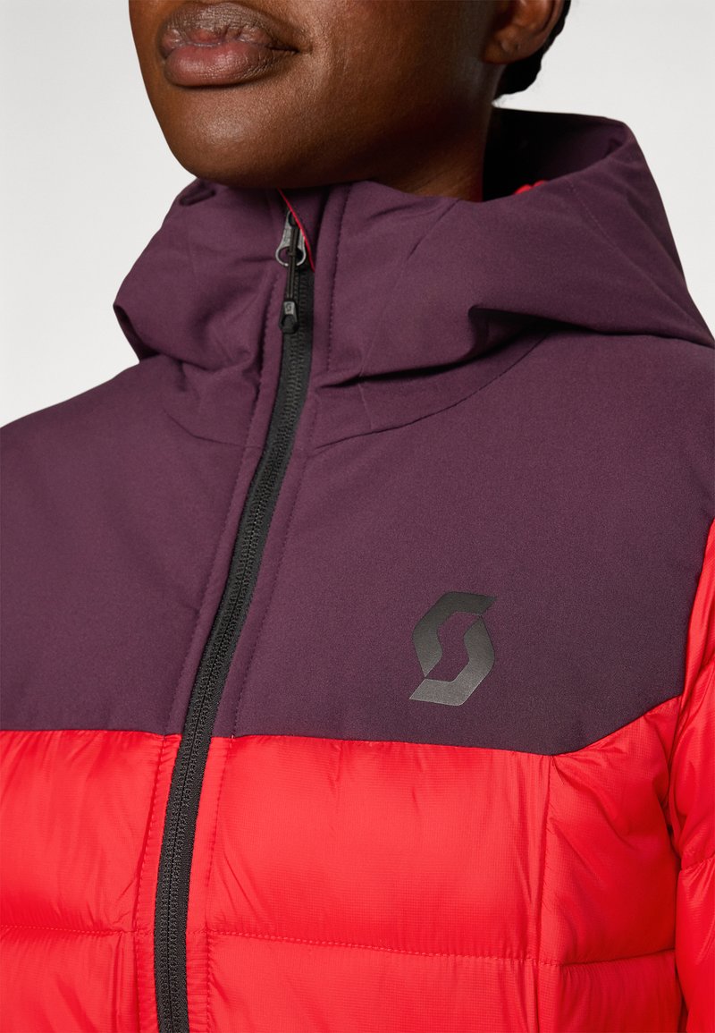 Czerwono-fioletowa kurtka puchowa z zapięciem na zamek, przypiętym kapturem i czarnym logo na klatce piersiowej. Gładka tekstura z ocieplającym wyściółką.