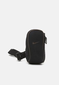 Černá taška na zip Nike s elegantním designem, nastavitelným popruhem a subtilním hnědým logem.