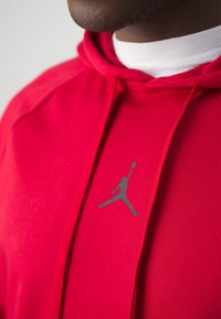 Sweat à capuche rouge en mélange de coton avec un logo Jumpman gris, des cordons de serrage, et un col côtelé. Texture lisse, avec une coupe ajustée.