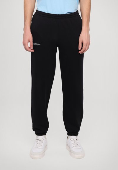 Black sweatpants made of soft material, featuring an elastic waistband, tapered leg design, and a small graphic detail on the front.