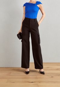 Top azul ajustado con diseño off-shoulder, combinado con pantalones cargo negros de pierna ancha y cintura alta, que presentan bolsillos frontales y una textura suave.