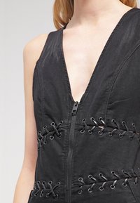 Mono sin mangas negro con escote en V profundo, con cremallera frontal y detalles de cordones en los laterales. Hecho de tejido texturizado.