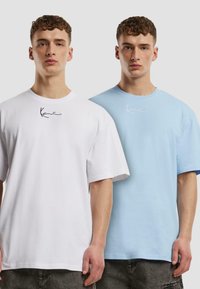 Deux T-shirts à manches courtes, l'un blanc et l'autre bleu clair, tous deux avec un logo noir près de l'encolure. Matière en coton, coupe ample.