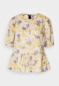 Blouse ample avec manches courtes bouffantes, encolure fendue avec lien, ourlet à volants, et imprimé floral jaune et violet sur tissu blanc.