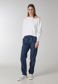 Weiße Baumwoll-Sweatshirt, lockerer Schnitt, gerippte Bündchen, kombiniert mit dunkelblauen Jogginghosen, elastischer Bund und lockere Silhouette. Weiße Sneaker.
