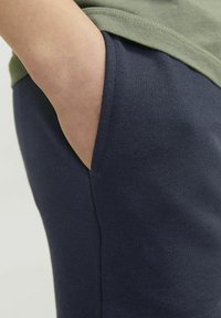 Pantalones de chándal azul marino con un bolsillo lateral, hechos de una suave mezcla de algodón, con una textura lisa y un diseño ajustado.