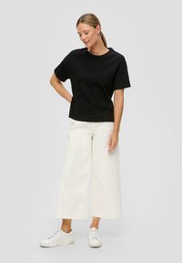 Zwart korte mouwen top met gestructureerde strepen, gecombineerd met off-white wijde broek en witte sneakers, wat een casual outfit creëert.