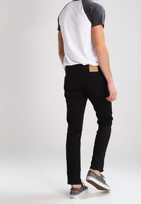 Mustat slim fit -farkut, harmaa ja valkoinen raglan-t-paita sekä harmaat tennarit valkoisilla pohjilla. Vyötäröllä näkyy ruskea nahkainen merkki.