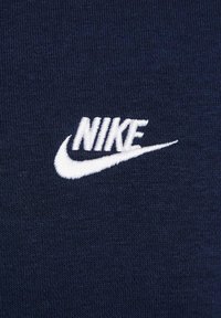Un tessuto blu navy con una texture liscia presenta un logo Nike ricamato di bianco, che mostra il famoso design a swoosh del brand.