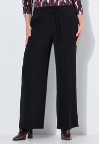 Brede zwarte broek met een trekkoord in de taille, gemaakt van gladde stof. Gecombineerd met glanzende bordeauxkleurige haklaarzen.