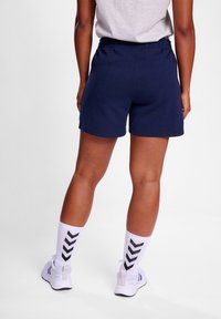 Calções de algodão azul-marinho com um cós elástico, combinados com meias brancas com padrões de chevron pretos e sapatilhas.