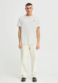 T-shirt en coton gris clair avec un petit graphique de citron jaune, associé à un pantalon large écru et des chaussures noires. Design simple, coupe décontractée.