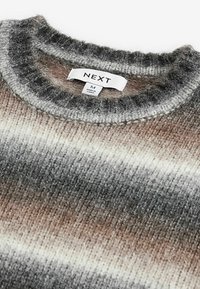 Pull en maille douce avec des rayures horizontales gris, beige et blanc, avec une étiquette au col indiquant NEXT taille M, fabriqué en Chine.