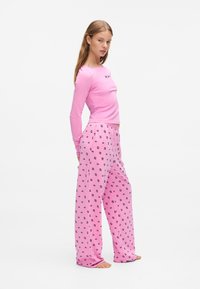 Langsleeve roze top met een ronde hals, gecombineerd met roze pyjamabroek met een zwart patroon. Zacht materiaal, losse pasvorm en een elastische tailleband.