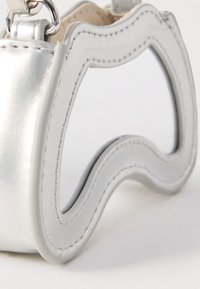 Stříbrná kabelka s obdélníkovým zrcadlem se zvlněnými okraji, připevněným kovovým kroužkem na bílém pozadí.