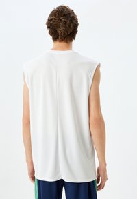 Witte mouwloze sporttop met een ronde halslijn en een gladde, lichte textuur. De achterkant heeft een subtiele naaddetails, zonder versieringen.