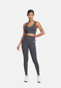 Szara sportowa biustonosz i legginsy wykonane z elastycznego materiału, posiadające dopasowany krój, gładką teksturę i małe akcenty logo.