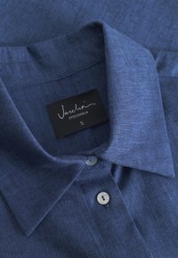 Mörkblå knapp-up skjorta i texturerad tyg, med en klassisk krage, en knapp vid halsen och en etikett som säger "Vaschaï Stockholm S."