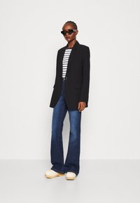 Svart skreddersydd blazer over en hvit og marineblå stripet topp, kombinert med utsvingte blå jeans og off-white klogs. Inkluderer stilige, rektangulære solbriller.