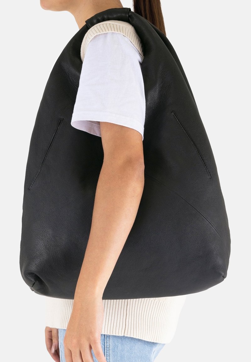 Bolso de cuero negro con una forma redondeada y de tamaño exagerado. Presenta acentos de punto en color marrón claro en la parte superior y dos bolsillos laterales para mayor comodidad.