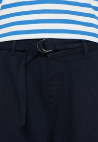 Mörkblå jeans med en texturerad yta, som har bälteshällor och ett matchande tygbälte med en rund spänne. Randig blå och vit skjorta ovanför.