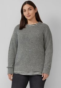 Grijze gebreide trui met een ribbelstructuur, ronde halslijn en lange mouwen. Een gestreept shirt is eronder gedragen.