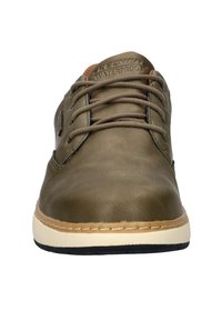 Scarpa impermeabile verde oliva con texture liscia, punta tonda, lacci marroni e suola beige. Presenta logo impresso sulla linguetta e dettagli di cucitura.
