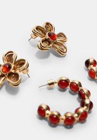 Ohrstecker und Creolen in Goldoptik mit floralen und abgerundeten Designs, verziert mit roten Cabochon-Steinen; beinhaltet einen Blumenstecker und geschwungene Creolen.