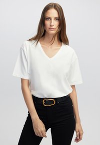Biała koszulka V-neck z krótkim rękawem, wykonana z gładkiego materiału. Zestawiona z czarnymi jeansami o wysokim stanie i czarnym paskiem z złotą klamrą.