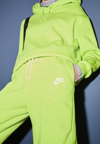 Neon grön Nike-hoodie med dragsko och ficka, kombinerad med matchande joggers som har "Nike Air"-logotypen i vitt. Mjuk, texturerad tyg.