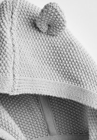 Tissu tricoté gris clair avec un motif de point texturé montrant une couture et un petit détail tricoté arrondi sur le dessus.