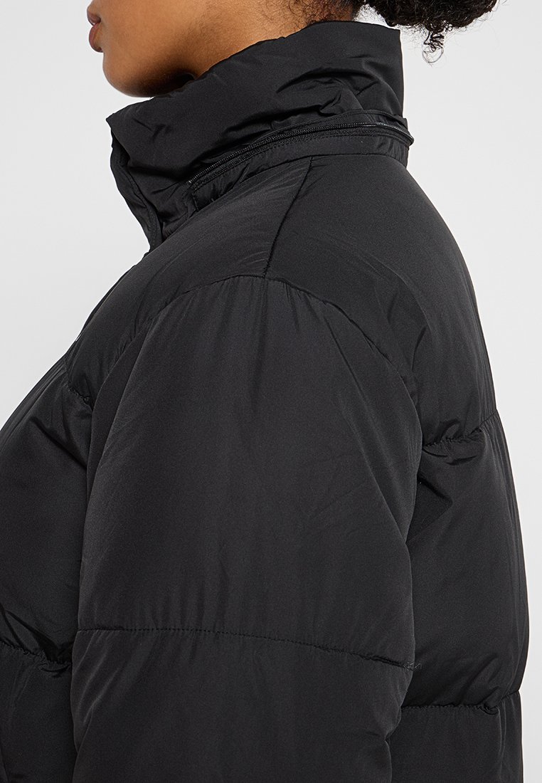 Zwarte pufferjack met een hoge kraag en ritssluiting. Glad oppervlak met een gestikte patroon, met een lichte glans. Beeld van de zijaanzicht.