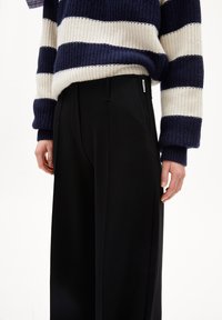 Knitted navy and white striped sweater with ribbed texture, paired with high-waisted black trousers featuring a side pocket and minimal detailing.