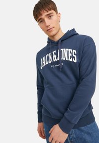 Granatowy bawełniany hoodie z przednią kieszenią typu kangur, kapturem ze sznurkiem oraz białym logo "JACK&JONES". Posiada ribbowe mankiety i dół.