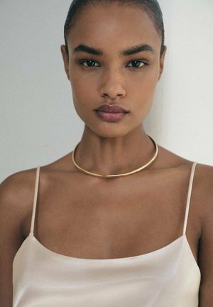 Collana choker in metallo dorato su una modella, caratterizzata da un design liscio e arrotondato; la modella indossa un top in satin leggero.