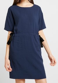 Mörkblå klänning med texturerad yta, korta ärmar och en justerbar midja med svarta satinband på varje sida.