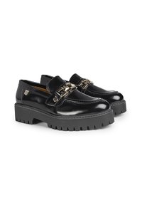 Mocasines de charol negro con suela de goma negra gruesa, que presentan un acento decorativo de eslabones metálicos en la parte superior.