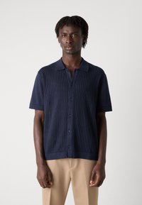 Polo shirt navy a maniche corte con texture a coste verticali, chiusura con bottoni e colletto a punta. Il tessuto appare morbido e leggero.
