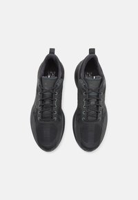 Černé sportovní boty s texturovaným síťovinovým svrškem, polstrovaným límcem a kontrastními šedými tkaničkami, s kulatou špičkou a lehkou podrážkou.